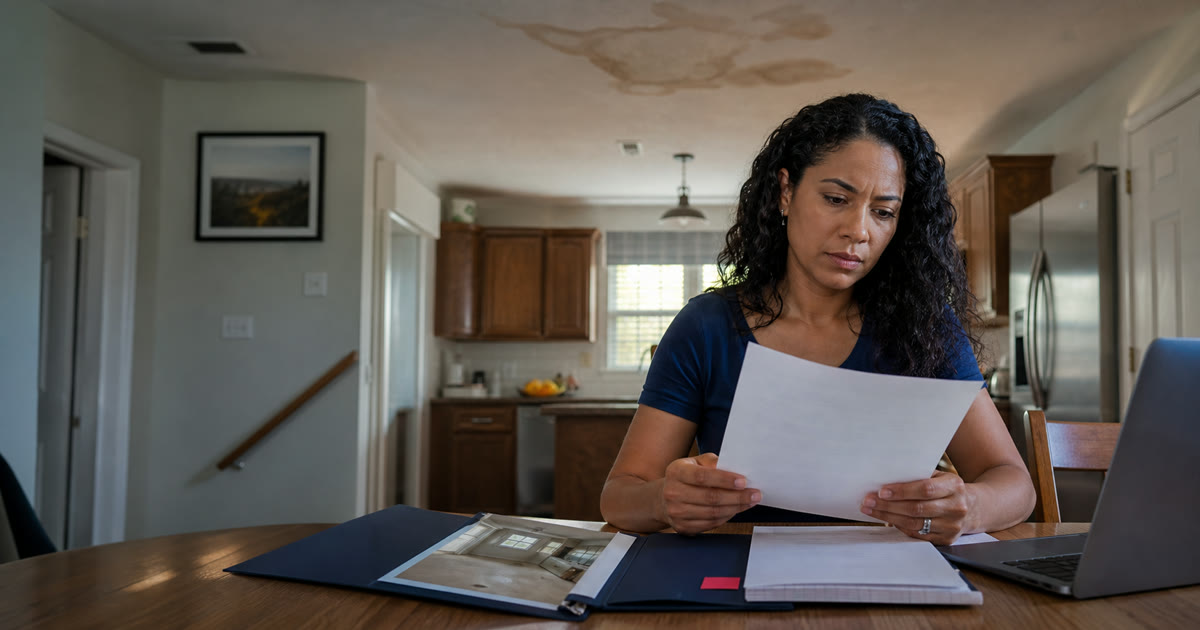 Homeowner reviewing an insurance claim decision beneath a water-stained ceiling
